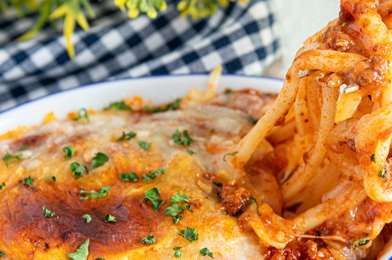 うどんを使った料理の皿があり、フォークで少し持ち上げられています。バックに花と飲み物。