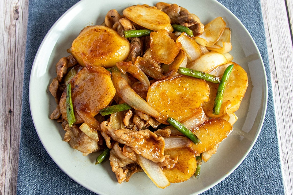 皿に盛られたじゃがいもと肉を使った料理。玉ねぎといんげんが混ざり、テーブルクロスの上に置かれている。