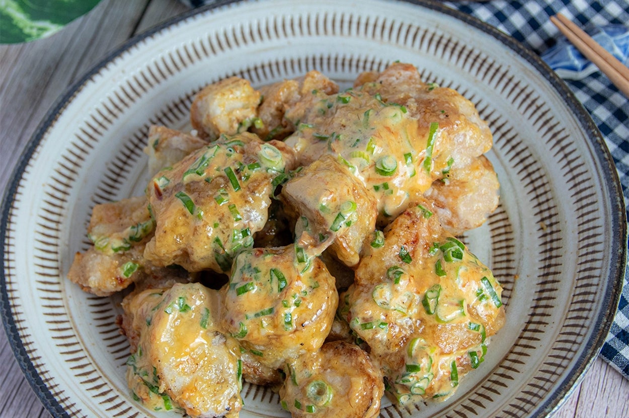 盛り付けられたクリーミーなソースがかかった里芋料理。木のテーブルと植物が背景に見える。