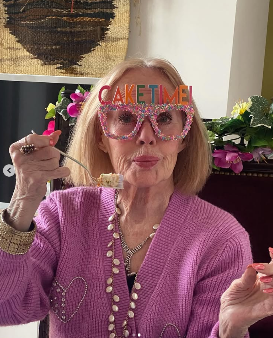 Tippi with "CAKE TIME!" glasses enjoys a forkful of cake, wearing a pink sweater adorned with heart patterns, accessorized with pearls
