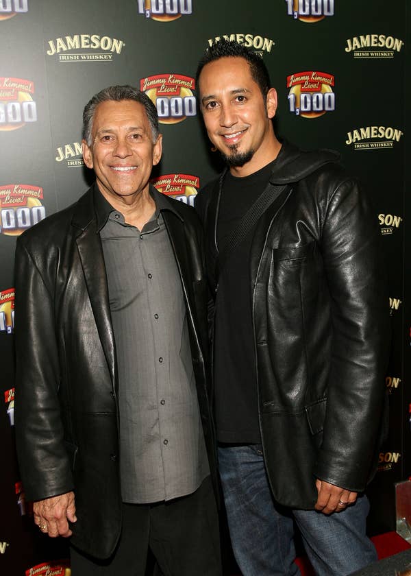 Two individuals on a red carpet, both wearing leather jackets, smiling towards the camera at an event