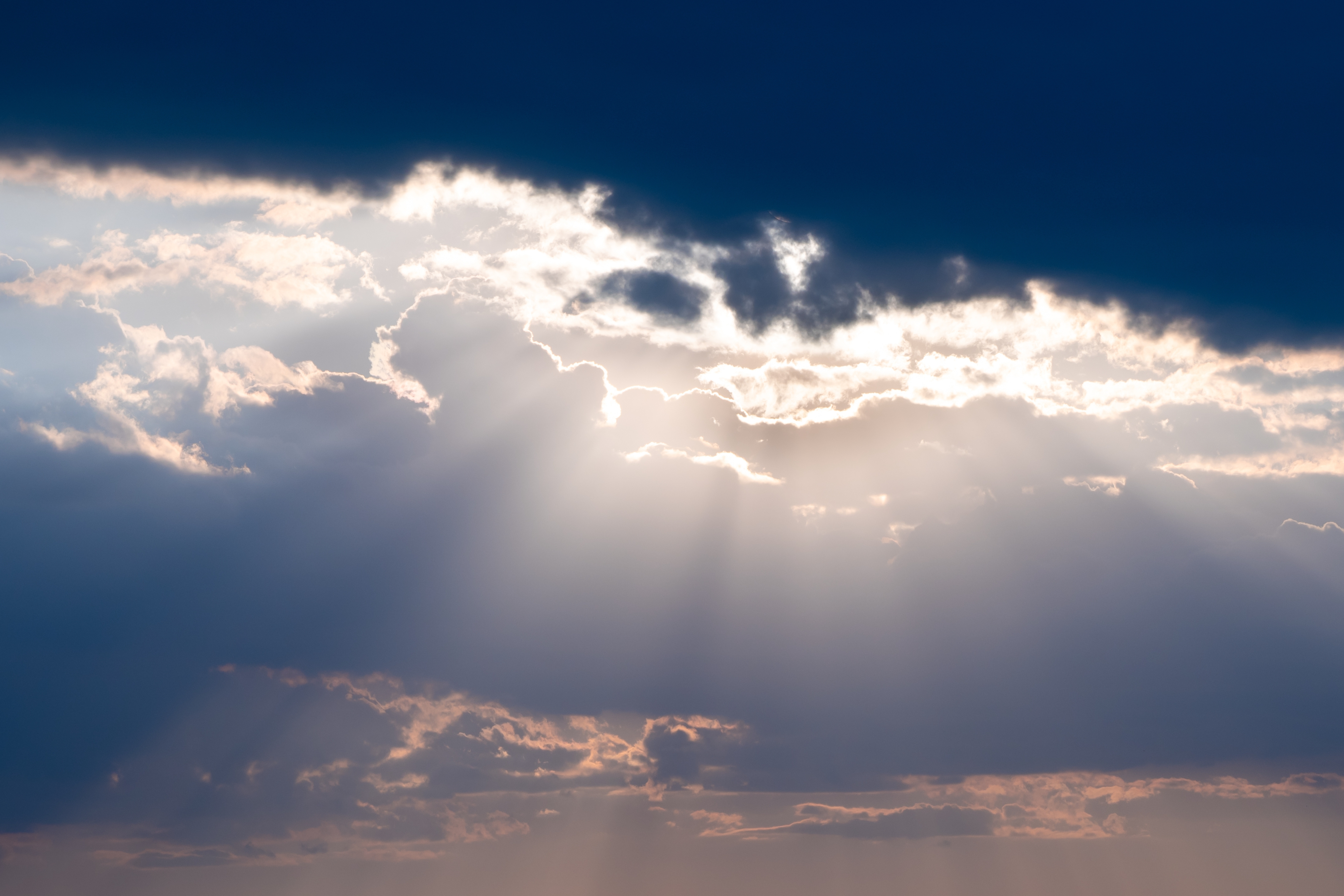 Solstråler bryter gjennom dramatiske skyer over et felt med vindturbiner i horisonten, og skaper et rolig og fengslende landskap