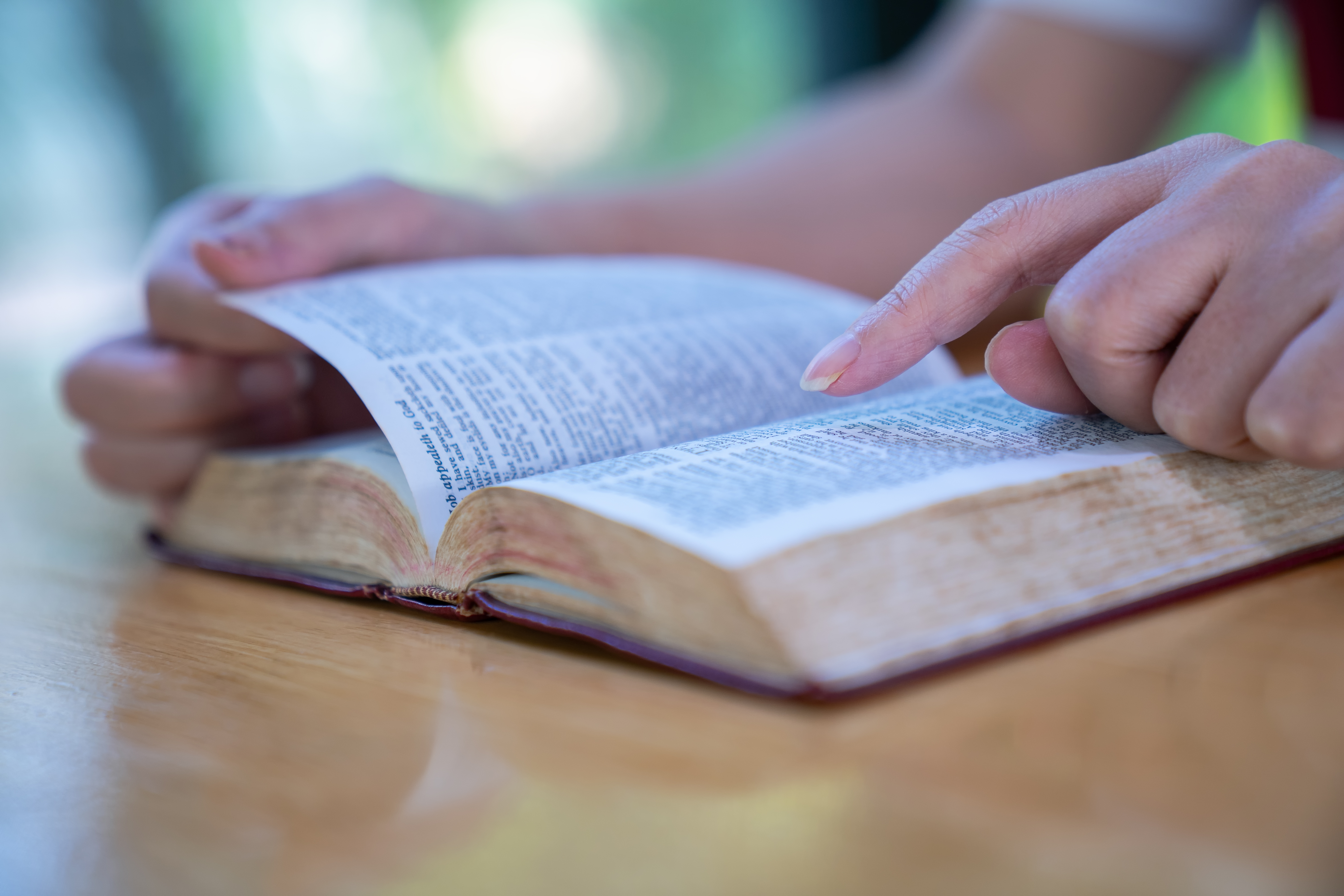 Person som leser en åpen bok på et bord, blar forsiktig gjennom sidene med fingeren etter teksten