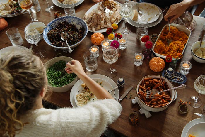People sharing a meal at a table with various dishes, including peas, carrots, and turkey. Candles and decorative pumpkins are on the table