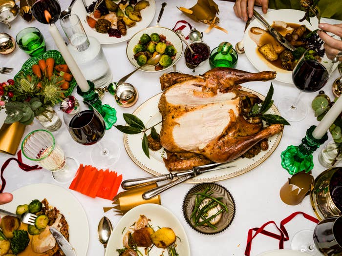 Festive dining table with a roasted turkey centerpiece, surrounded by plates of vegetables, wine glasses, and decorative table settings