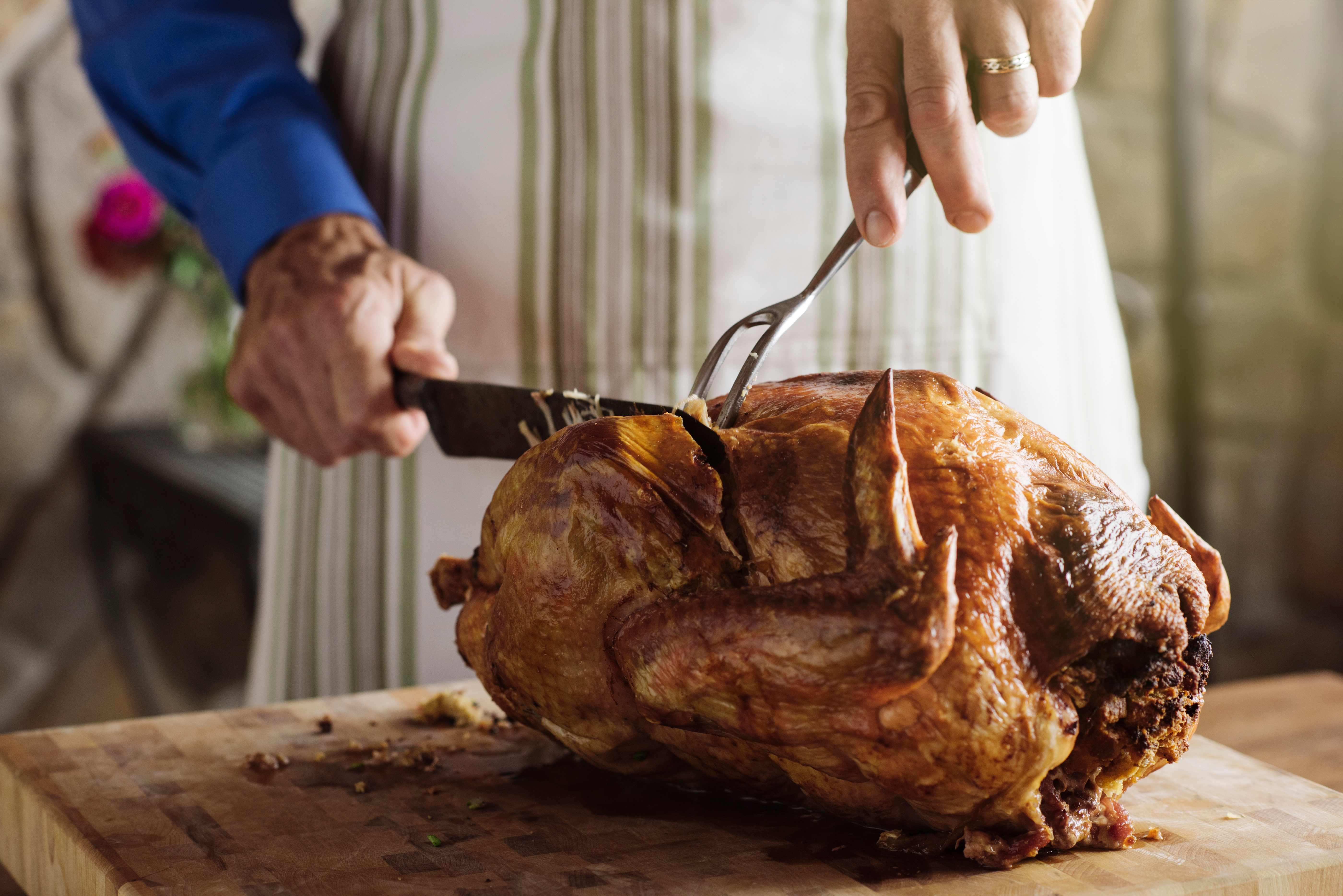 Person carving roasted turkey with a fork and knife on a wooden cutting board