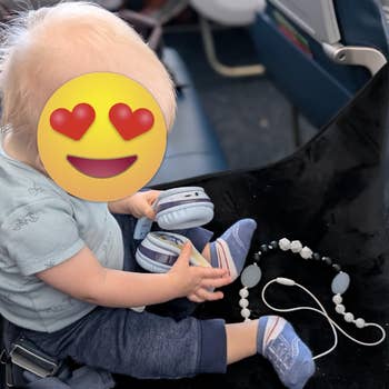 A babe connected an airplane spot plays with headphones and a pacifier clip portion wearing a airy garment and pants