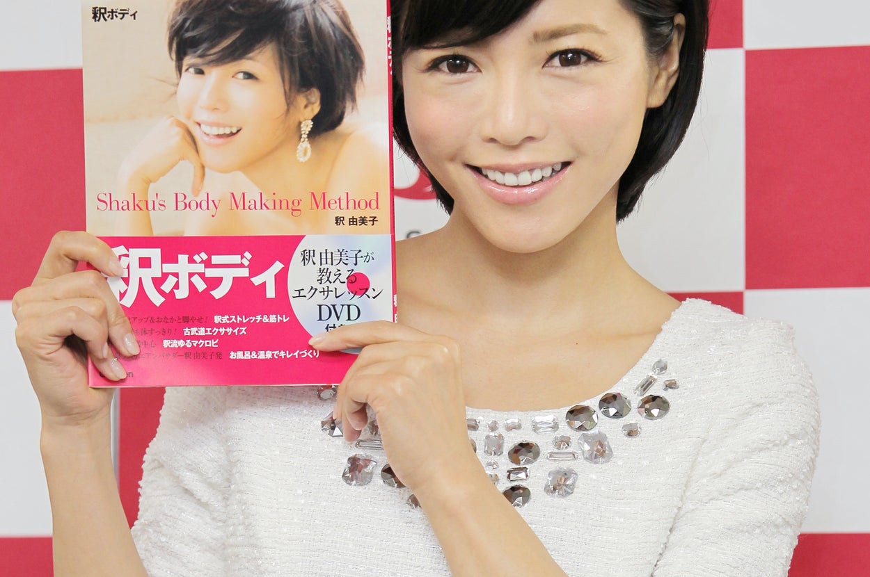 女性が白い服を着て、健康関連の本を紹介しています。