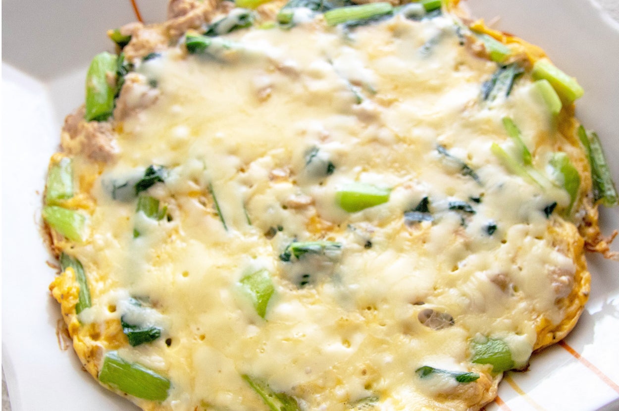 オムレツのような料理が四角い白い皿に載っている。野菜や緑の葉が混ざっている。