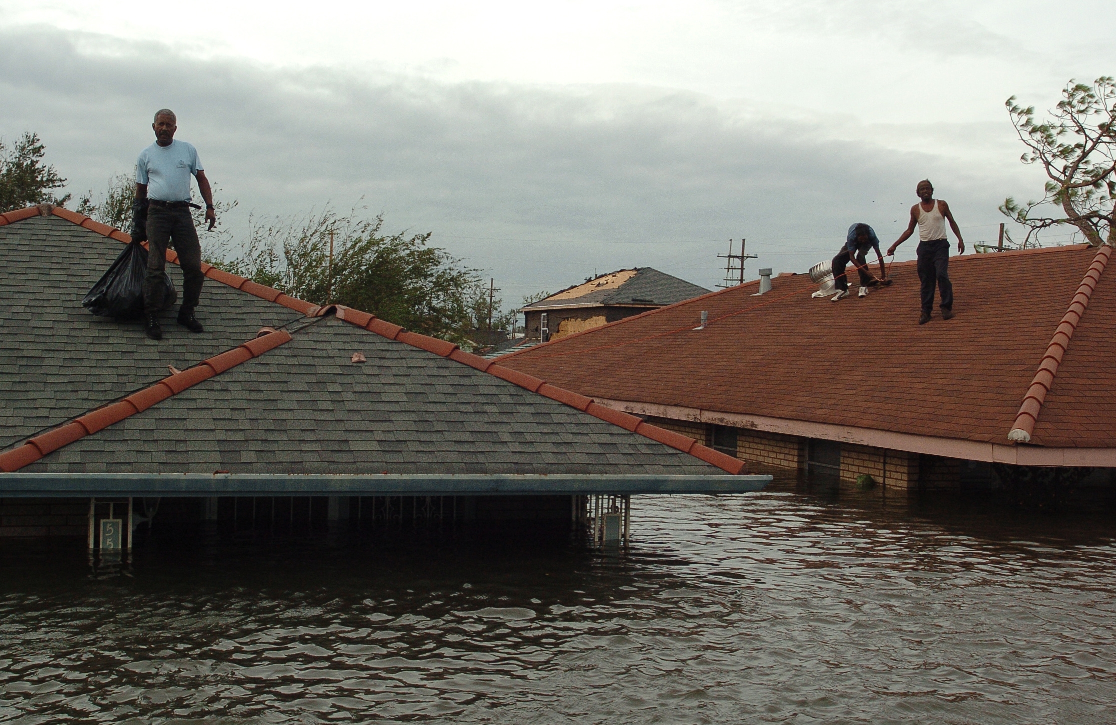 People lasting  connected  rooftops surrounded by floodwaters, with 1  idiosyncratic   holding a trash bag