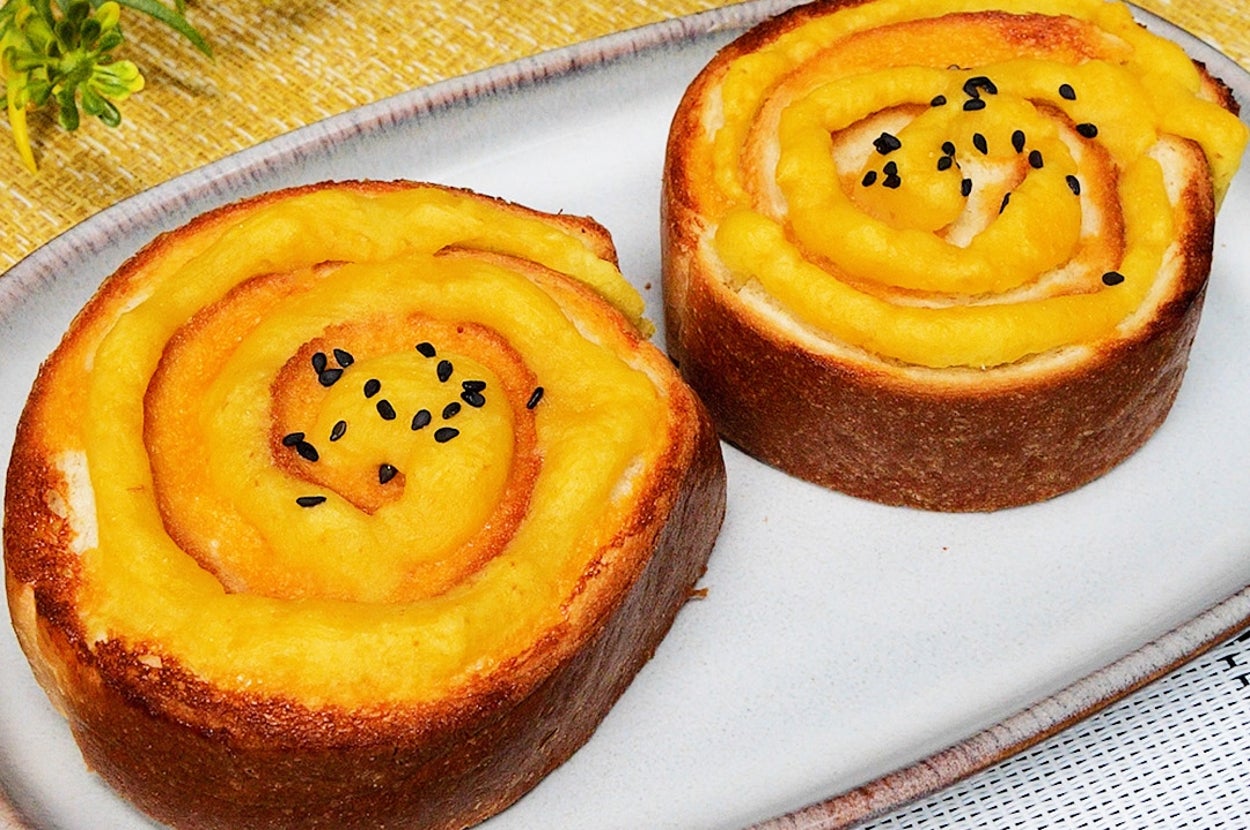 楕円形の皿に乗った2つのパン。花が背景にある。黒ゴマがトッピングされ、風味豊かに見える。