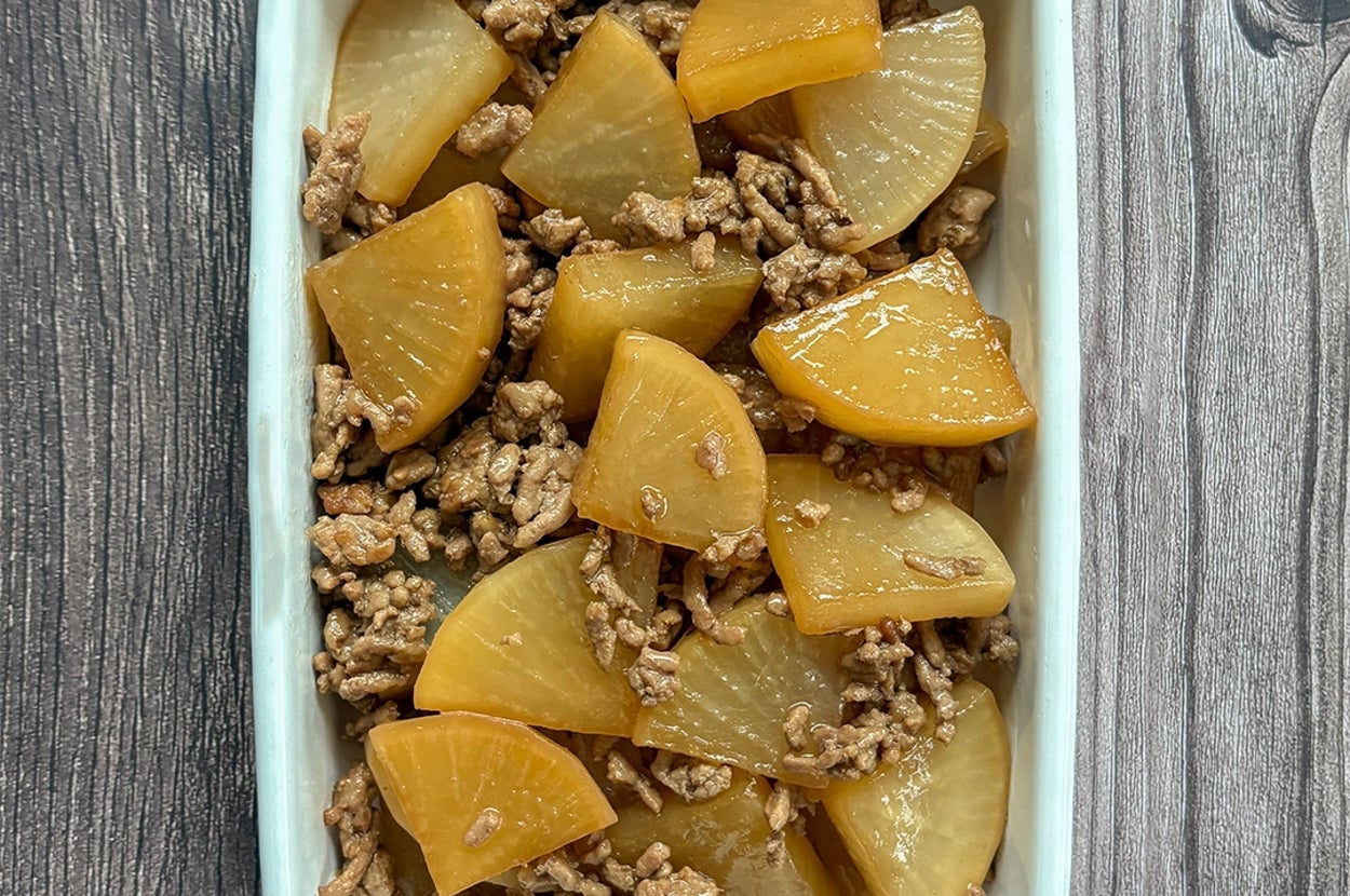 大根とひき肉の煮物が白い容器に盛られている。木目のテーブルに置かれている。