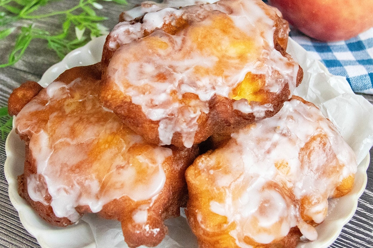 りんごのフリッターが皿に3つ置かれており、グレーズで覆われています。隣にりんごと装飾の葉があります。