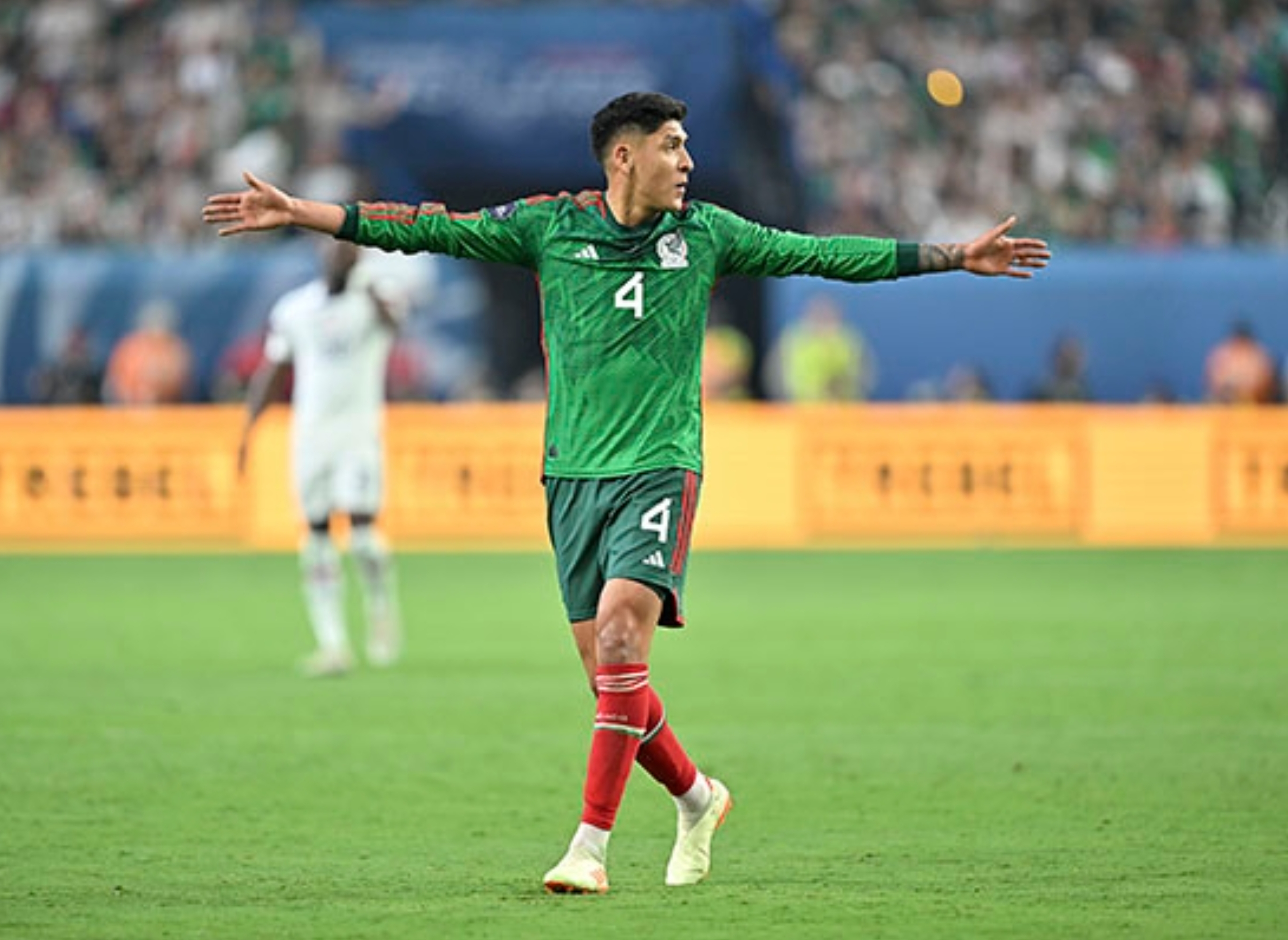 Soccer player in green jersey with number 4 gestures with arms wide open on a field during a match