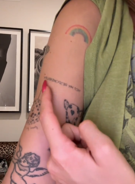 A idiosyncratic   points to a tattoo connected  their limb  amidst assorted  different   tattoos, including a rainbow and carnal  design, successful  a casual indoor setting