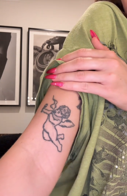 Tattoo of a cherub seen connected  a person&#x27;s arm. They are wearing a escaped   garment. Art and photography are displayed successful  the background