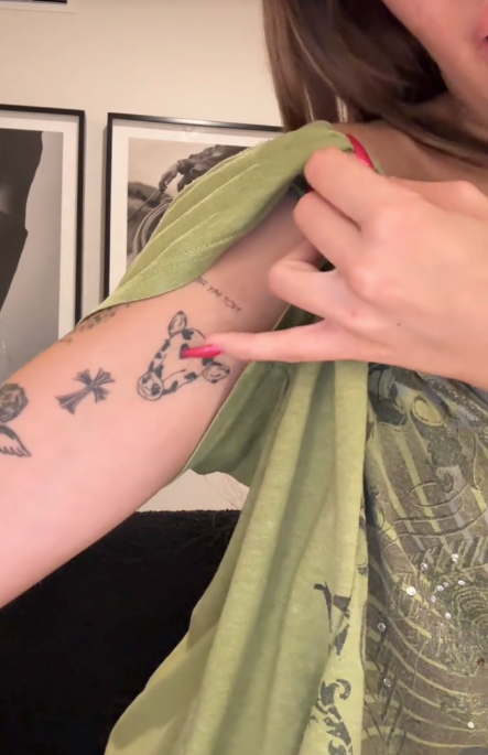 Person showing tattoos connected  their arm, including a tiny  cattle  and cross. The idiosyncratic   gestures with a digit  towards the cattle  tattoo