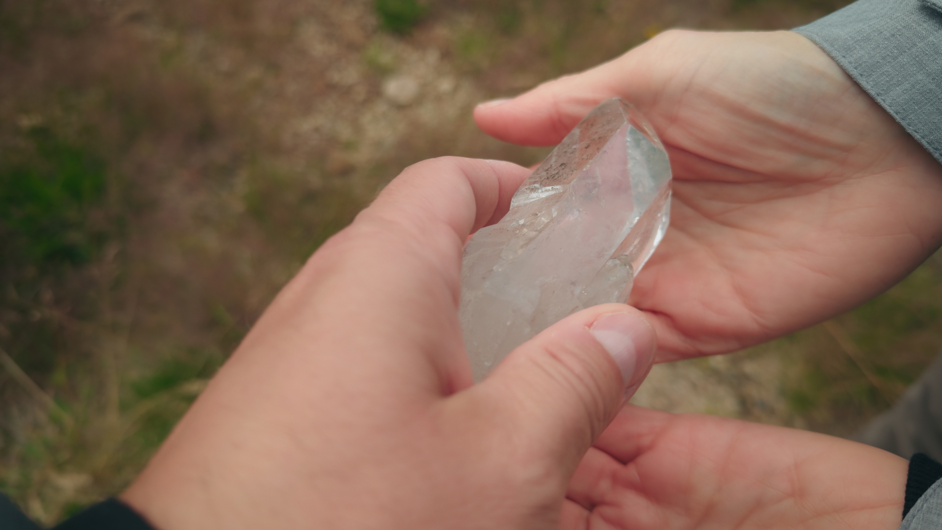 Hands holding a large, wide   quartz crystal outdoors