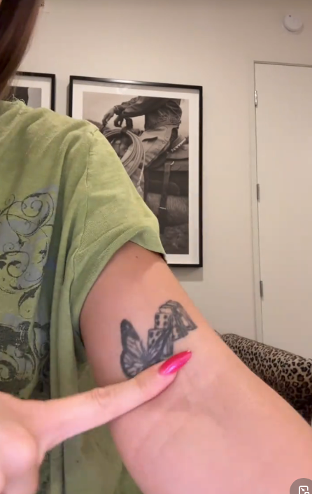 Close-up of a idiosyncratic   pointing to a butterfly tattoo connected  their arm, wearing a casual t-shirt. Art successful  the inheritance  features a idiosyncratic   with a camera