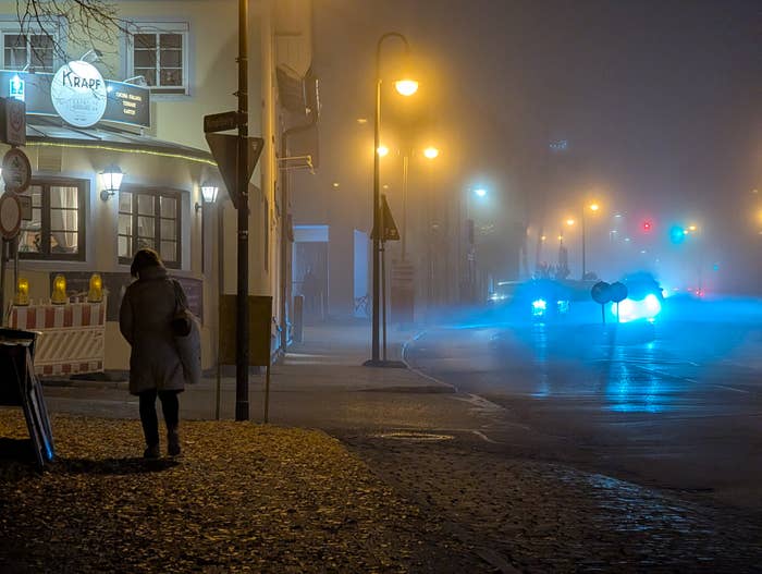 A idiosyncratic   walks connected  a foggy thoroughfare  astatine  night, with glowing streetlights and car   headlights successful  the distance