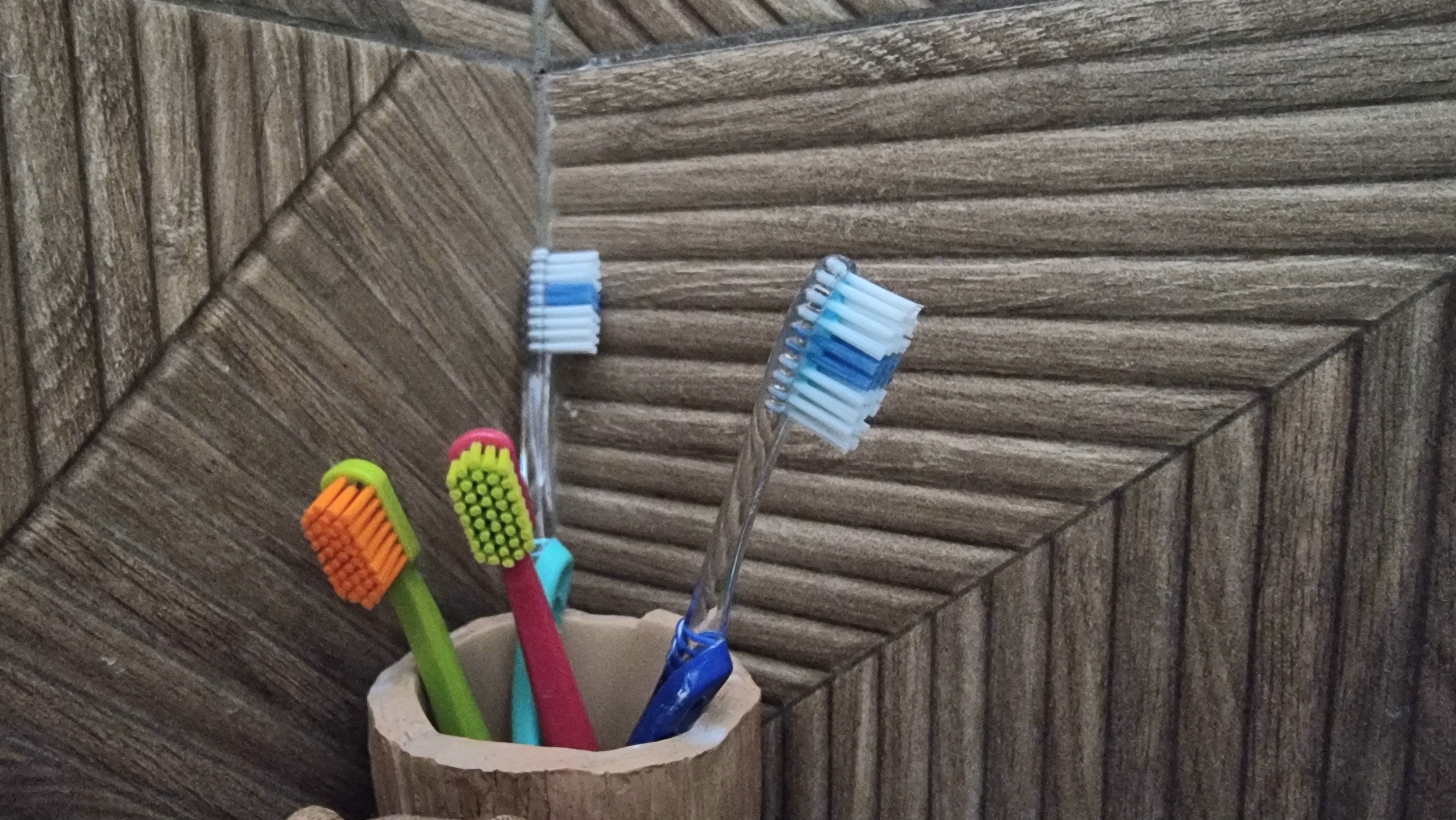 Fire tannbørster med fargerike bust står i en kopp mot en strukturert vegg