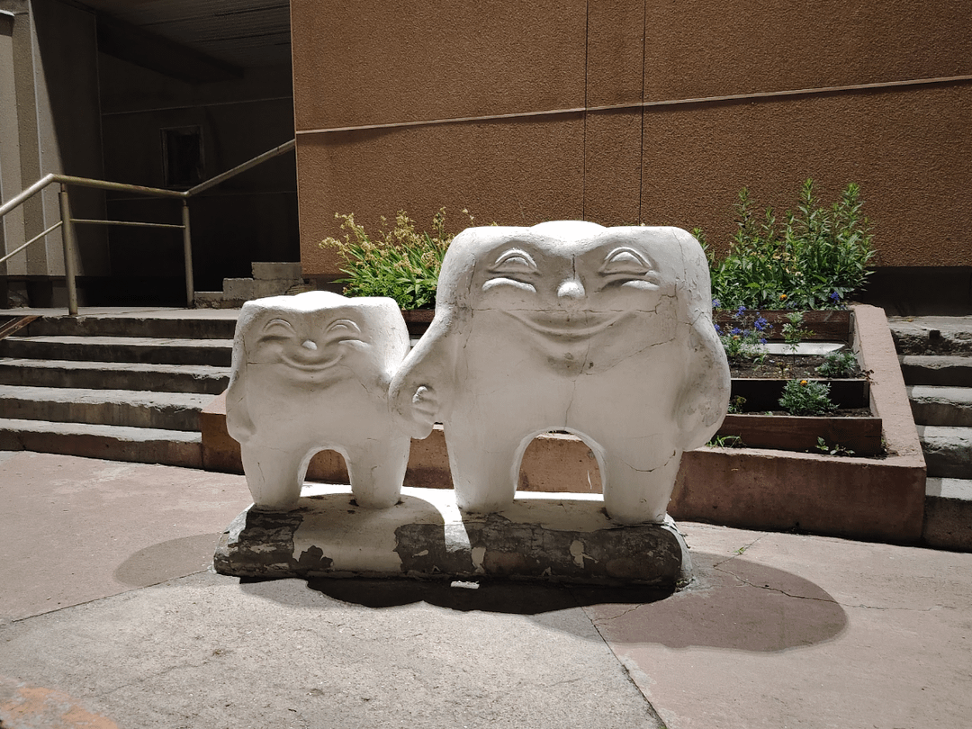 Two tooth-shaped sculptures with smiling faces basal   outdoors, holding hands