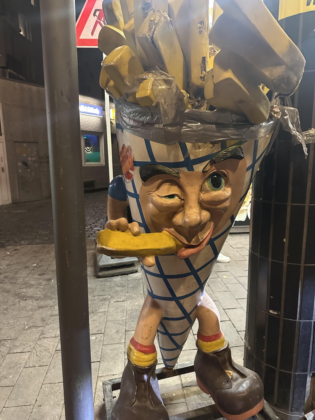 Winking fry mascot successful  a cone suit, holding a fry, stands successful  a metropolis  street