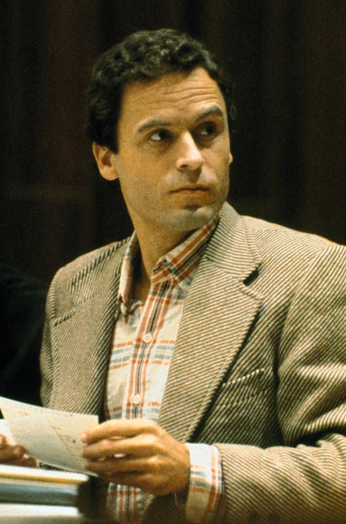 A person in a striped shirt and herringbone blazer holding papers, looking to the side in a formal setting