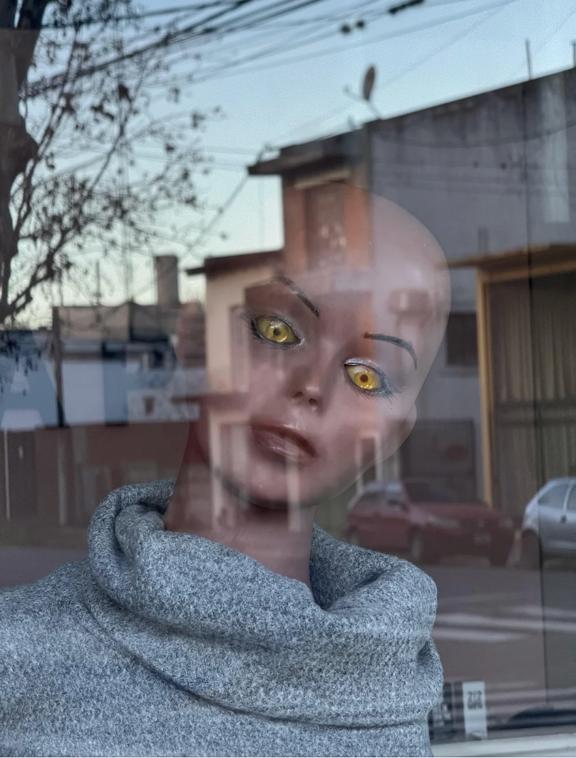 A mannequin with striking yellowish  eyes is reflected successful  a store  window, creating an eerie effect   with an municipality  thoroughfare  country   successful  the background