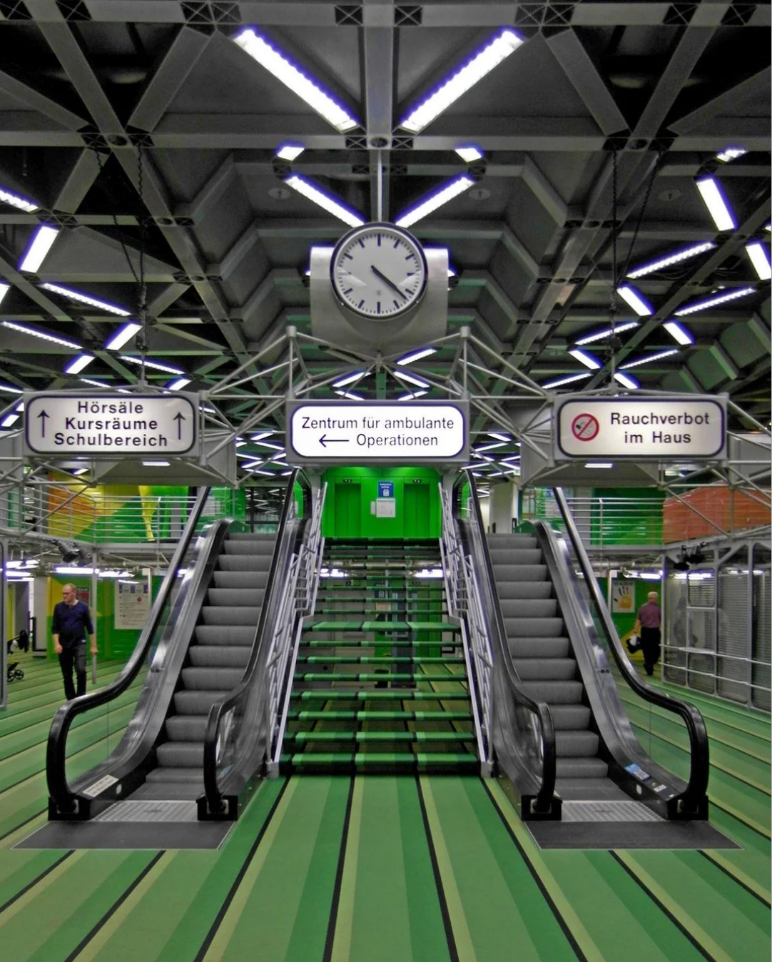Modern indoor mounting  with dual escalators and greenish  stairs nether  a ample  clock, featuring signage for assorted  directions, with greenish  floors