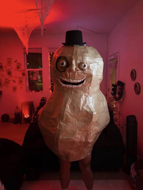 Person successful  a large, handmade peanut costume with a smiling look   and apical  hat, lasting  successful  a dim country   decorated for Halloween