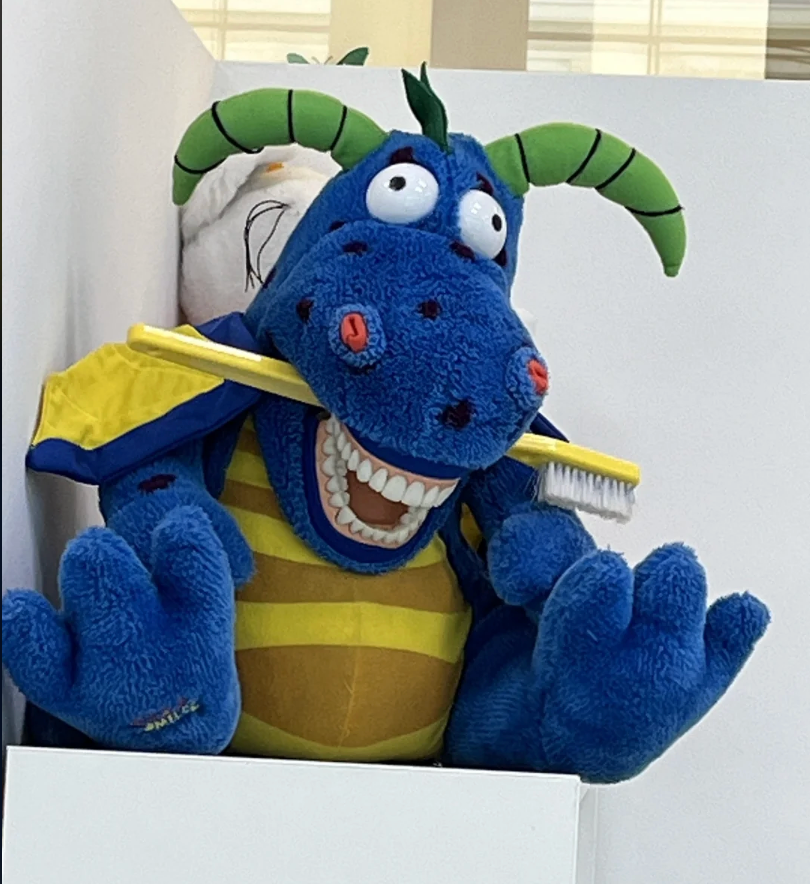 Large plush dragon mascot holding a toothbrush, wearing a striped costume with a affable  expression, connected  display