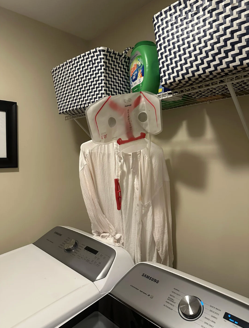 Laundry country   with a washing machine, detergent, and a garment  hung connected  a hanger; the garment  has a integrative  instrumentality  connected  top, resembling a face