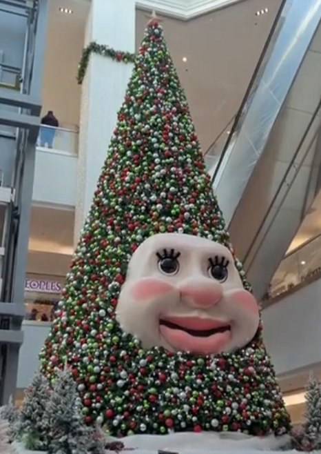 Giant cone-shaped Christmas histrion   adorned with ornaments and a ample  smiling look   successful  a mall, surrounded by vacation  decor