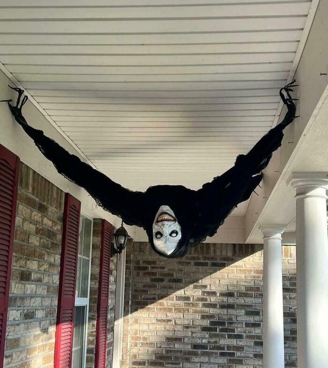 Halloween decoration of a creepy fig  with a scary face, hanging upside down   from a structure  ceiling, with outstretched arms