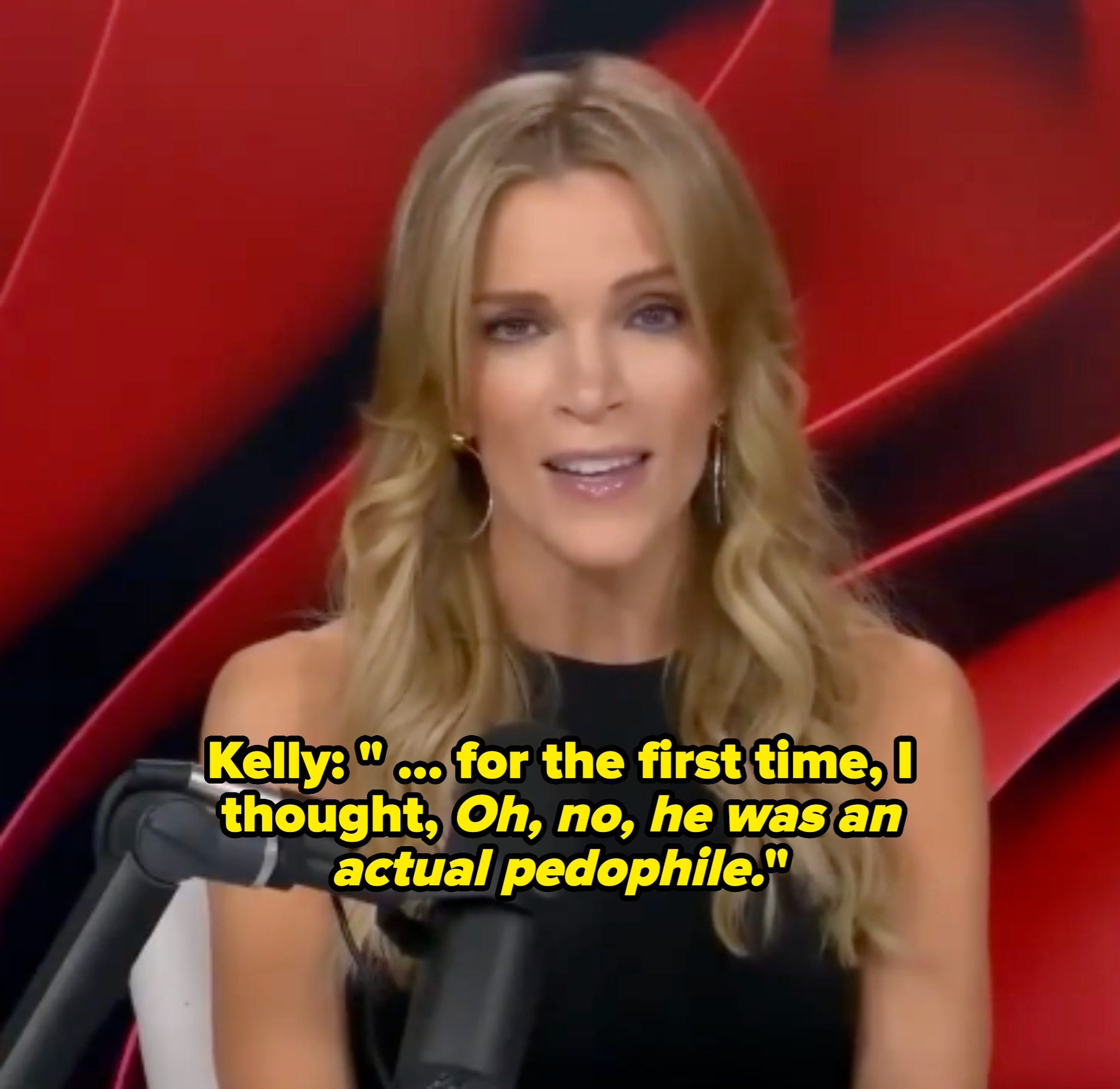 Person with long hair, wearing a sleeveless top, speaking into a microphone against a patterned backdrop