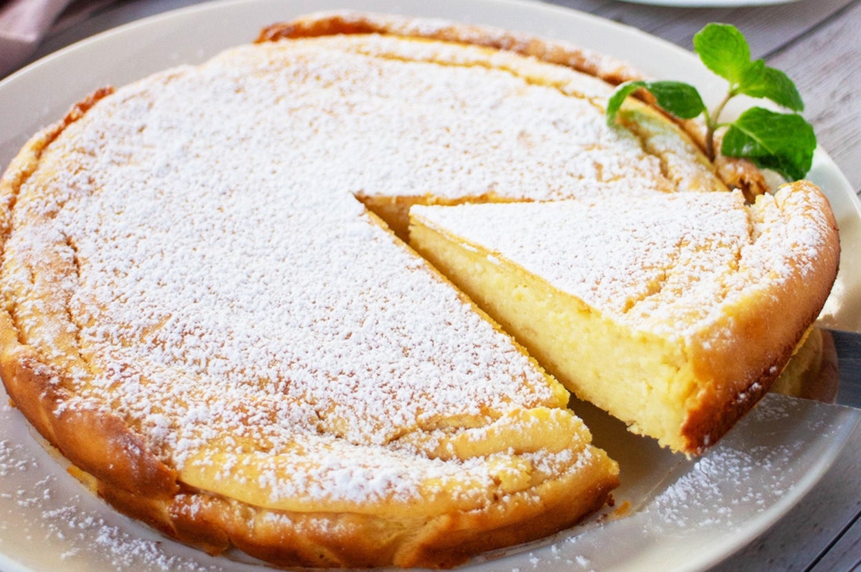 粉砂糖が振りかけられたチーズケーキのスライスが一切れと、奥に紅茶のカップがあるシーン。