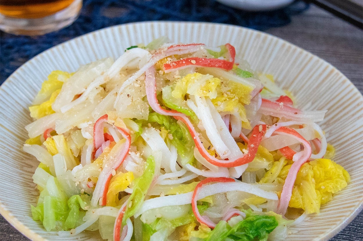 白菜とカニ風味かまぼこのナムルが盛り付けられている。背景に箸と飲み物。