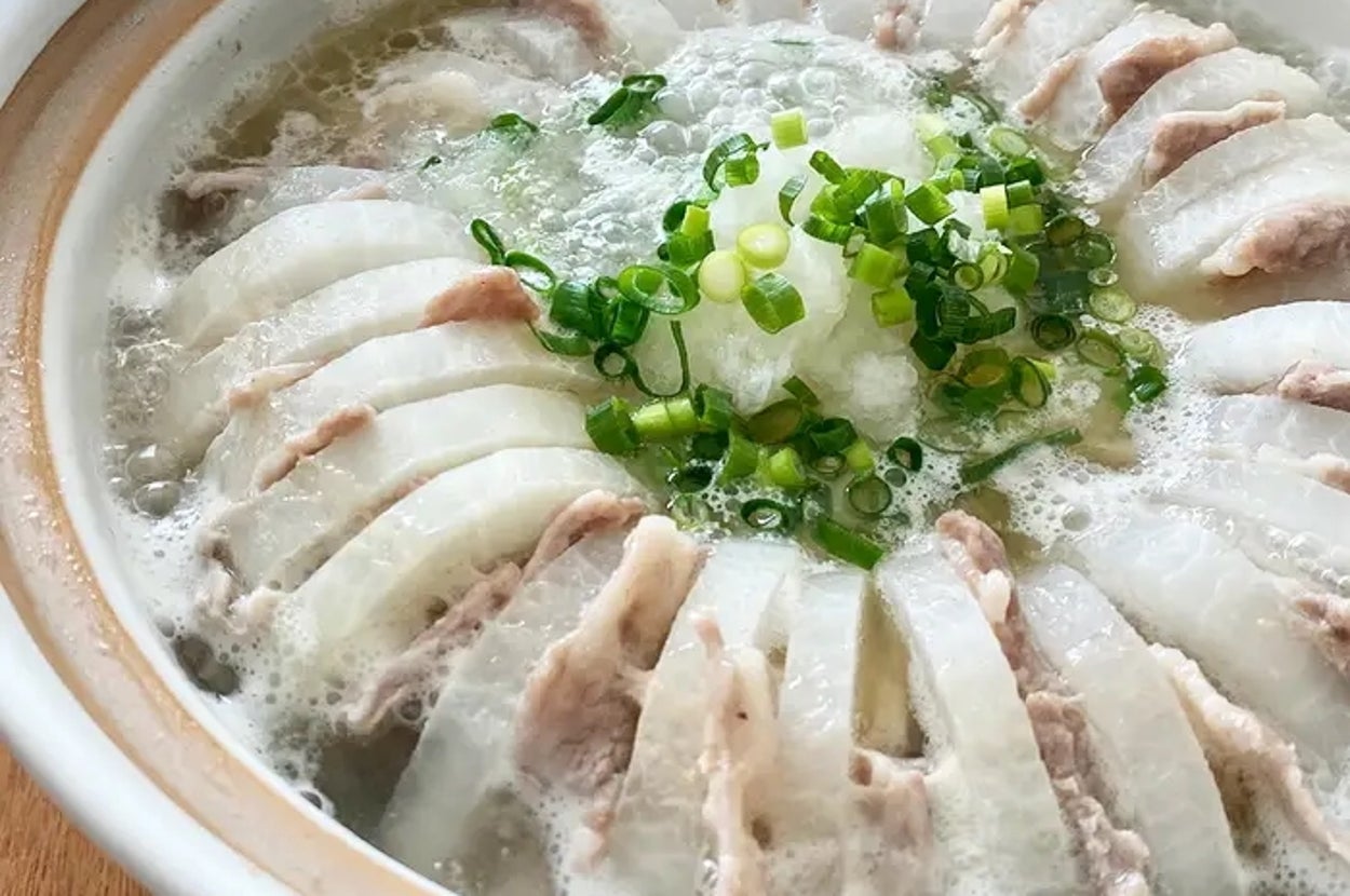 白い陶器の鍋に盛り付けられた豚肉と大根のスライス入りの鍋料理。上には刻んだネギがのっている。