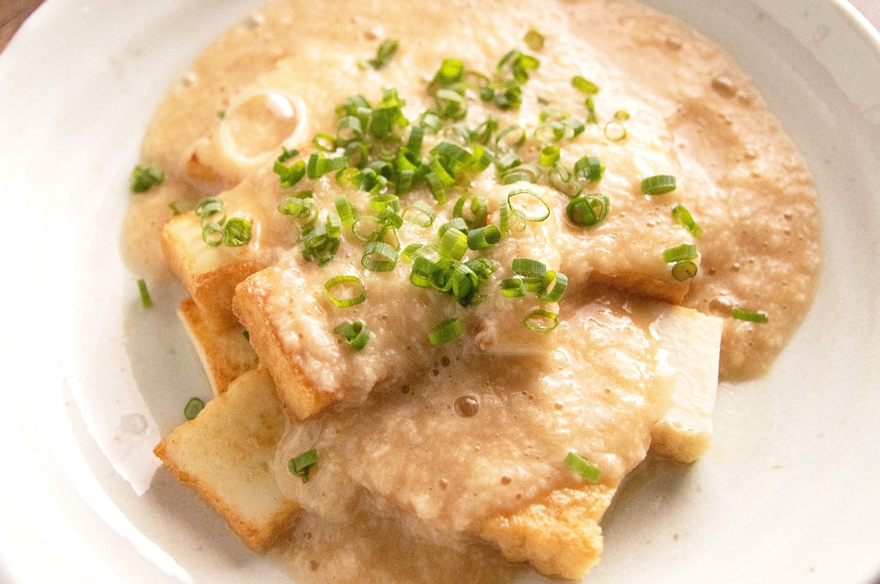 クリーミーなソースをかけた豆腐料理が皿に盛られ、ネギがトッピングされたおいしそうな一品。