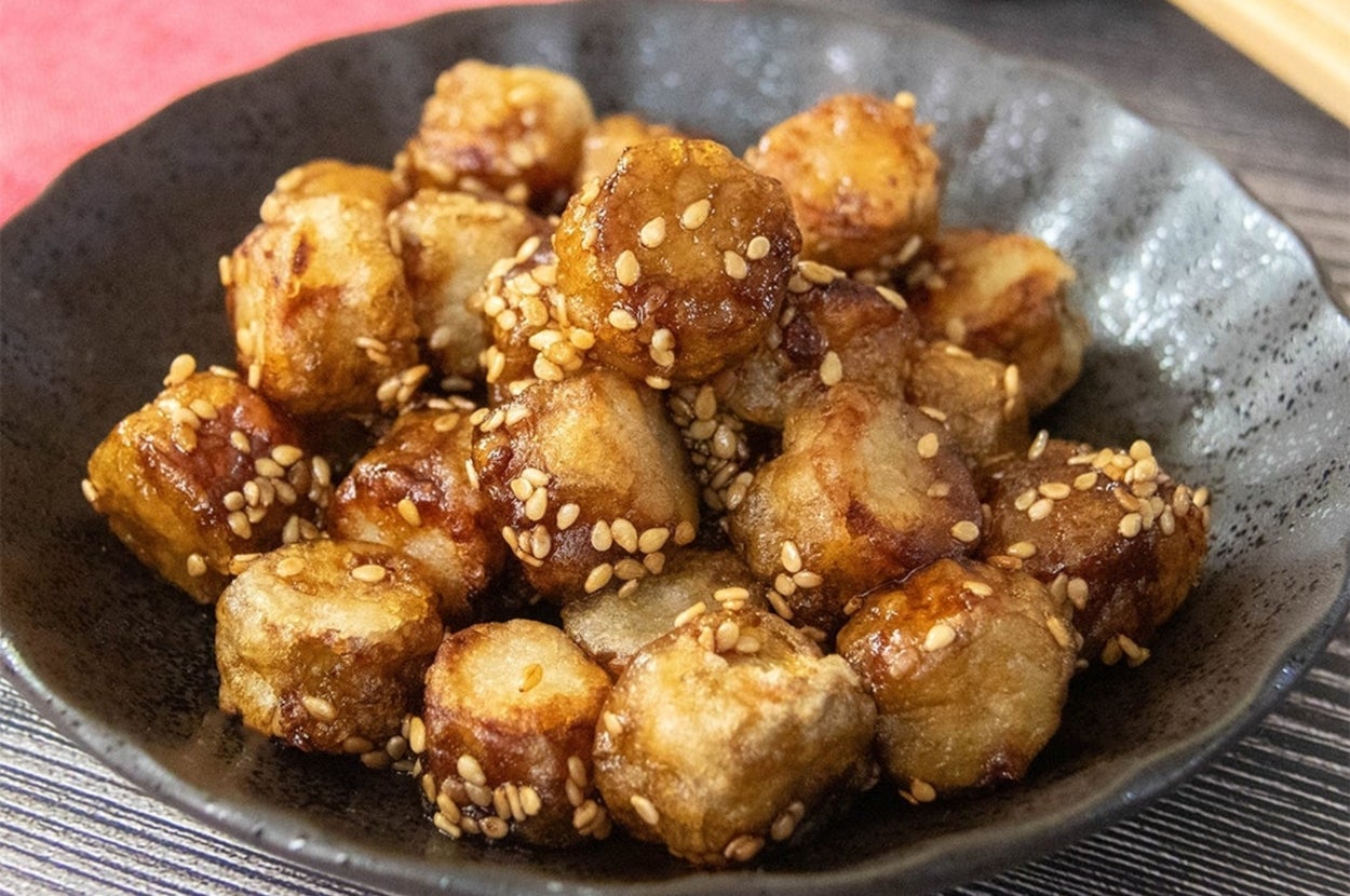 黒い皿に盛られたごまがまぶされた揚げ野菜の料理。背景に箸と布製の敷物が見える。