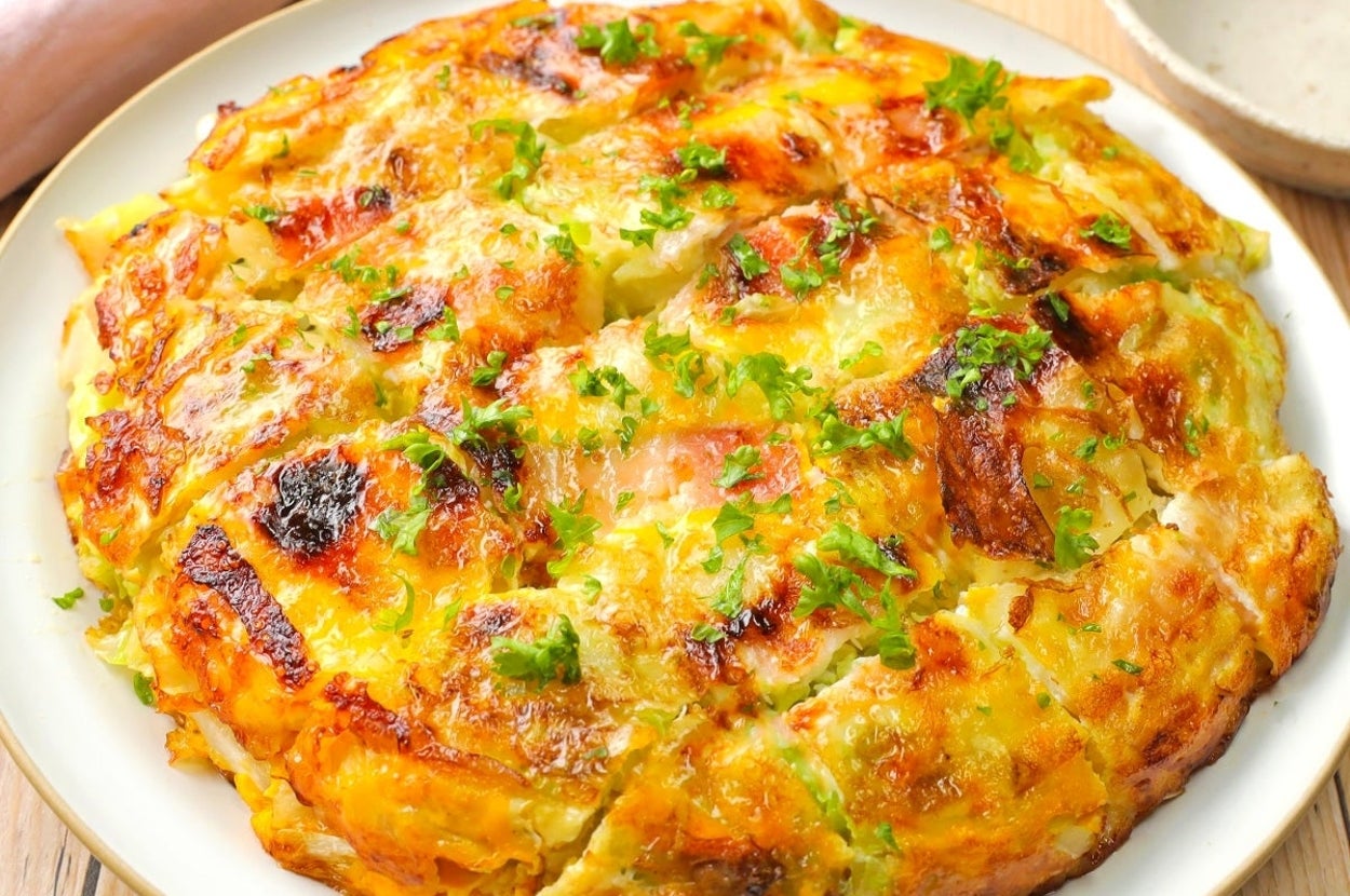 キャベツとチーズを使った焼き料理が白い皿に盛られている。周囲に緑のガーニッシュが散らされている。