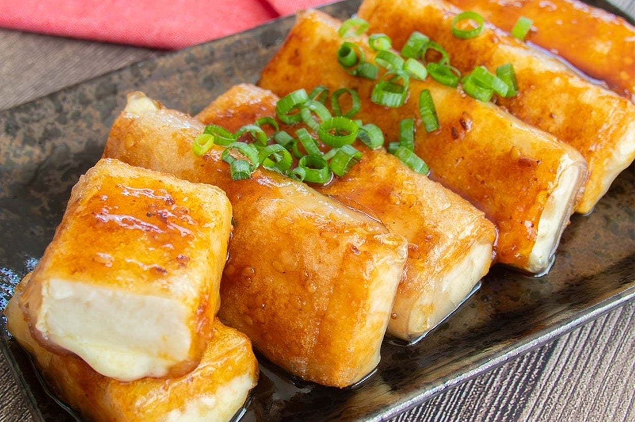 長方形のカリッと焼かれた豆腐が黒い皿に並び、ネギがトッピングされています。