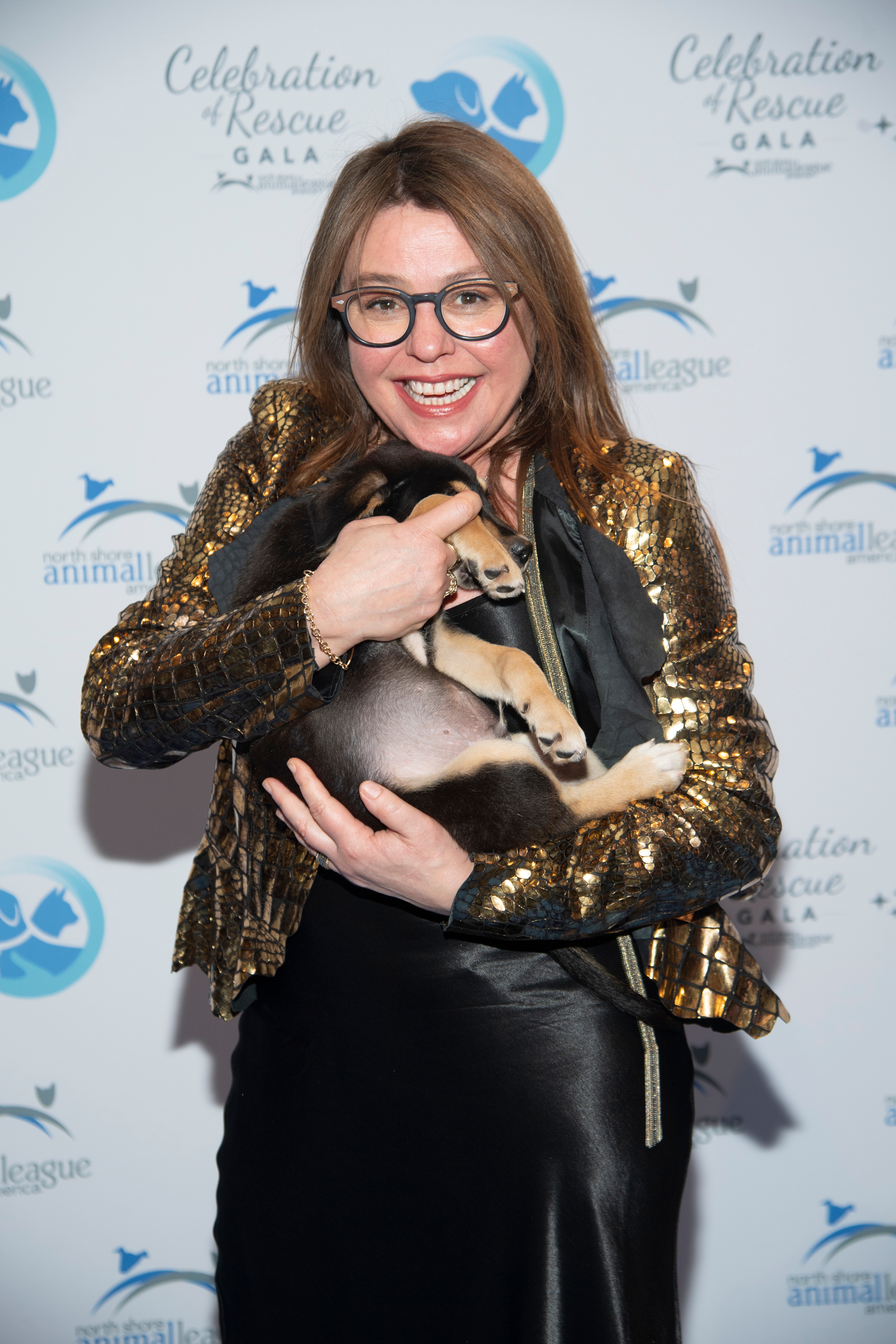 Celebrity connected a reddish carpet successful a shiny overgarment and achromatic skirt, smiling portion holding a puppy astatine an carnal rescue gala