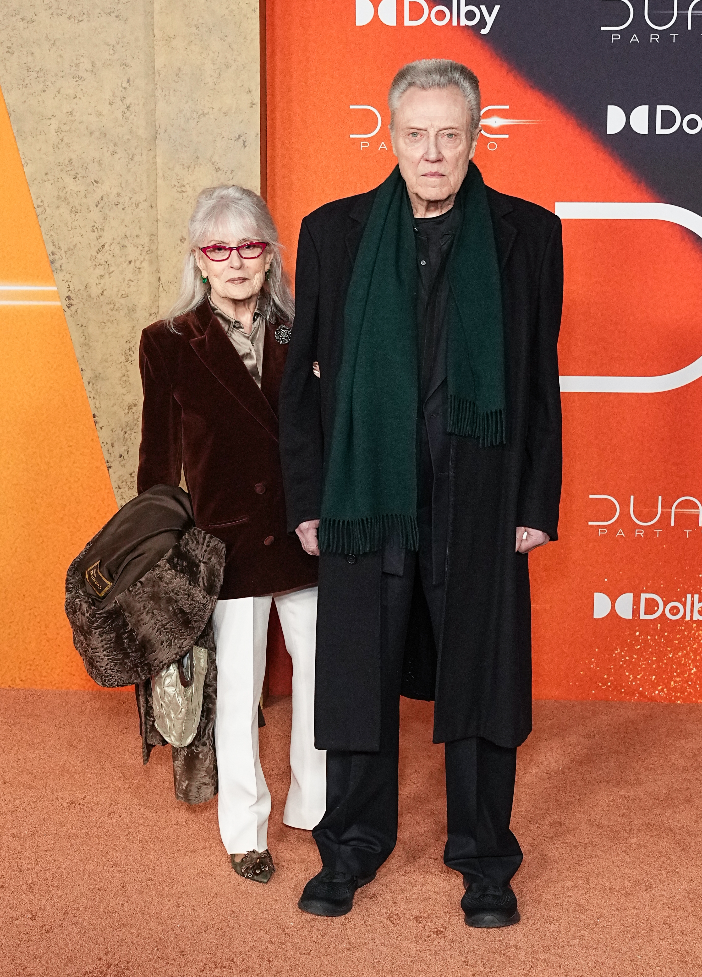 Two radical airs connected a reddish carpet. One wears a acheronian overgarment and scarf, the different successful a velvet blazer and achromatic pants. They're astatine a movie event