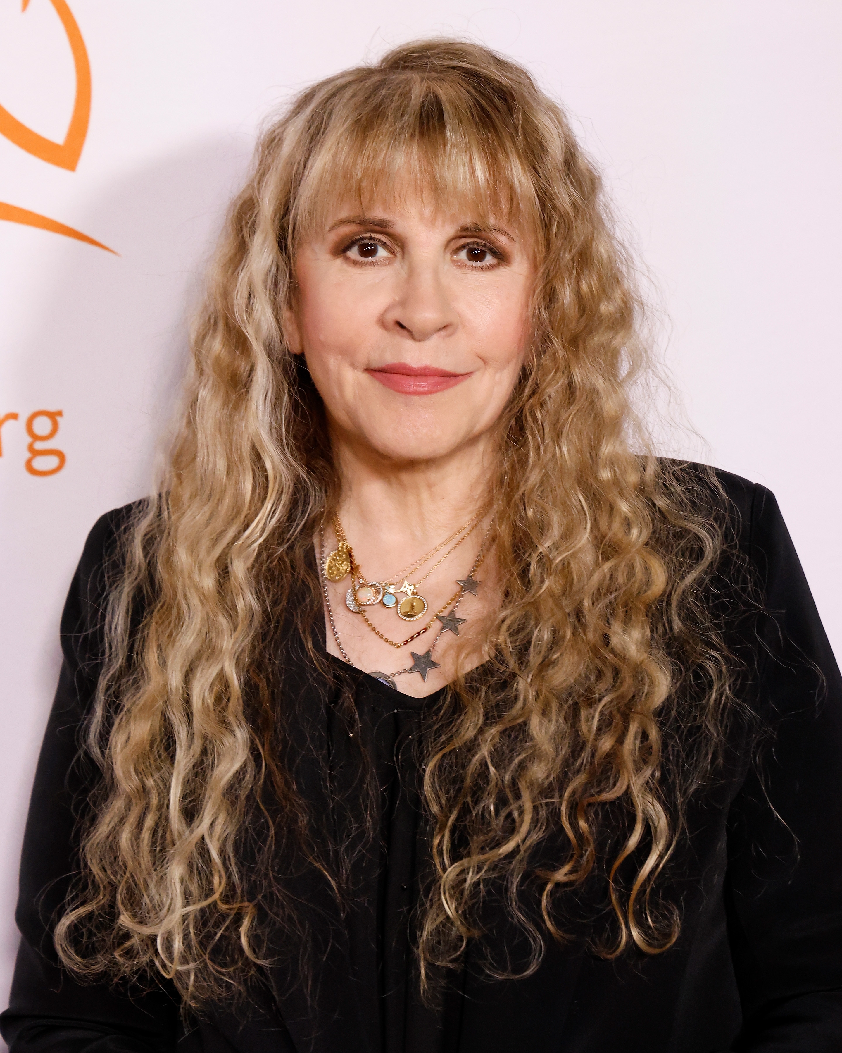 Person with long, wavy hairsbreadth wearing a achromatic outfit and layered necklaces, astatine a personage event