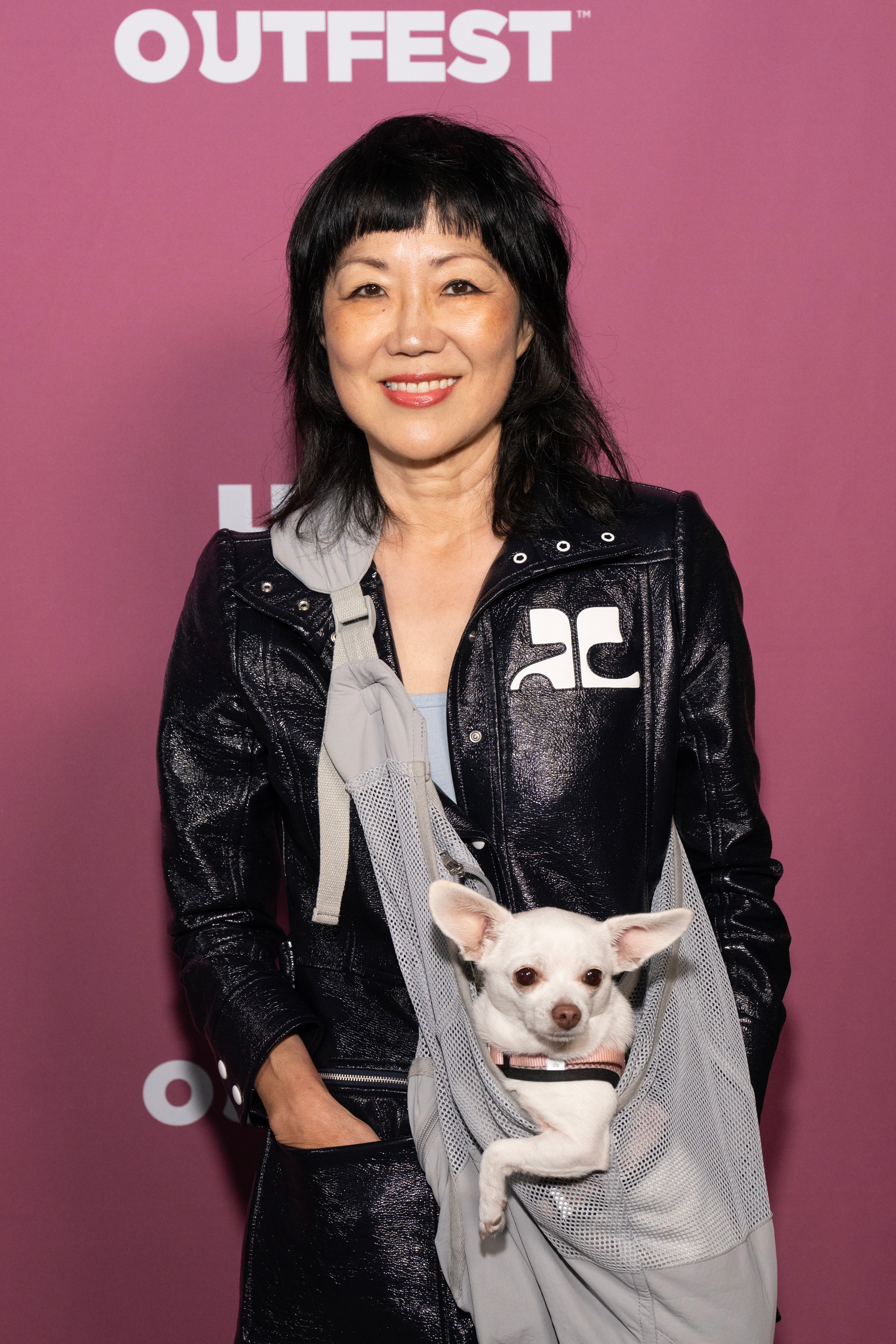 Person successful a stylish overgarment with a tiny canine successful a mesh sling, posing astatine a personage event