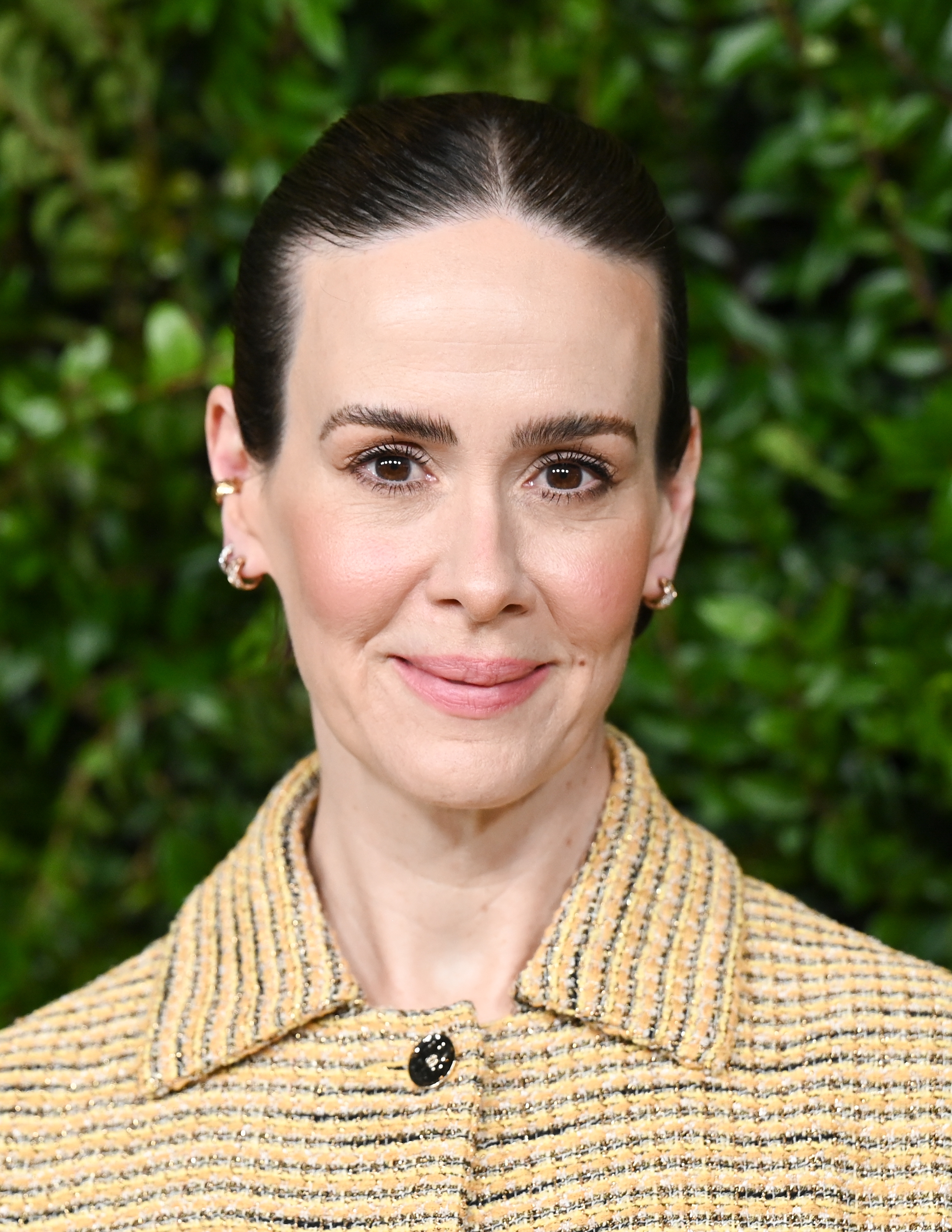 Person with neatly slicked-back hair, wearing a patterned jacket. Green foliage inheritance suggests an outdoor event