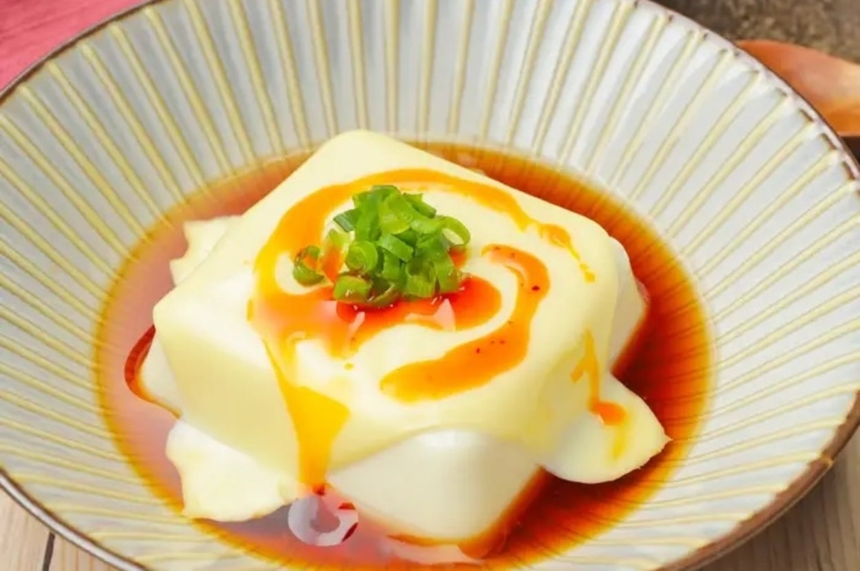 豆腐の上にネギが載り、醤油とラー油がかかった料理が皿に盛られている。