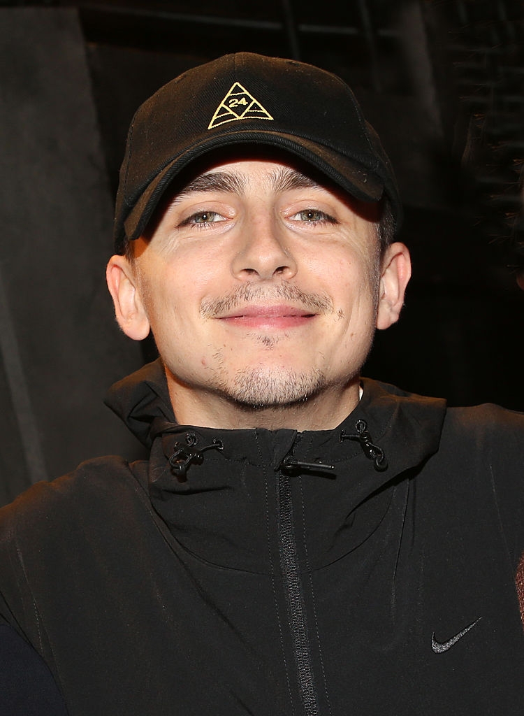 Person smiling, wearing a achromatic headdress and overgarment with a subtle logo connected the cap, looking straight astatine the camera